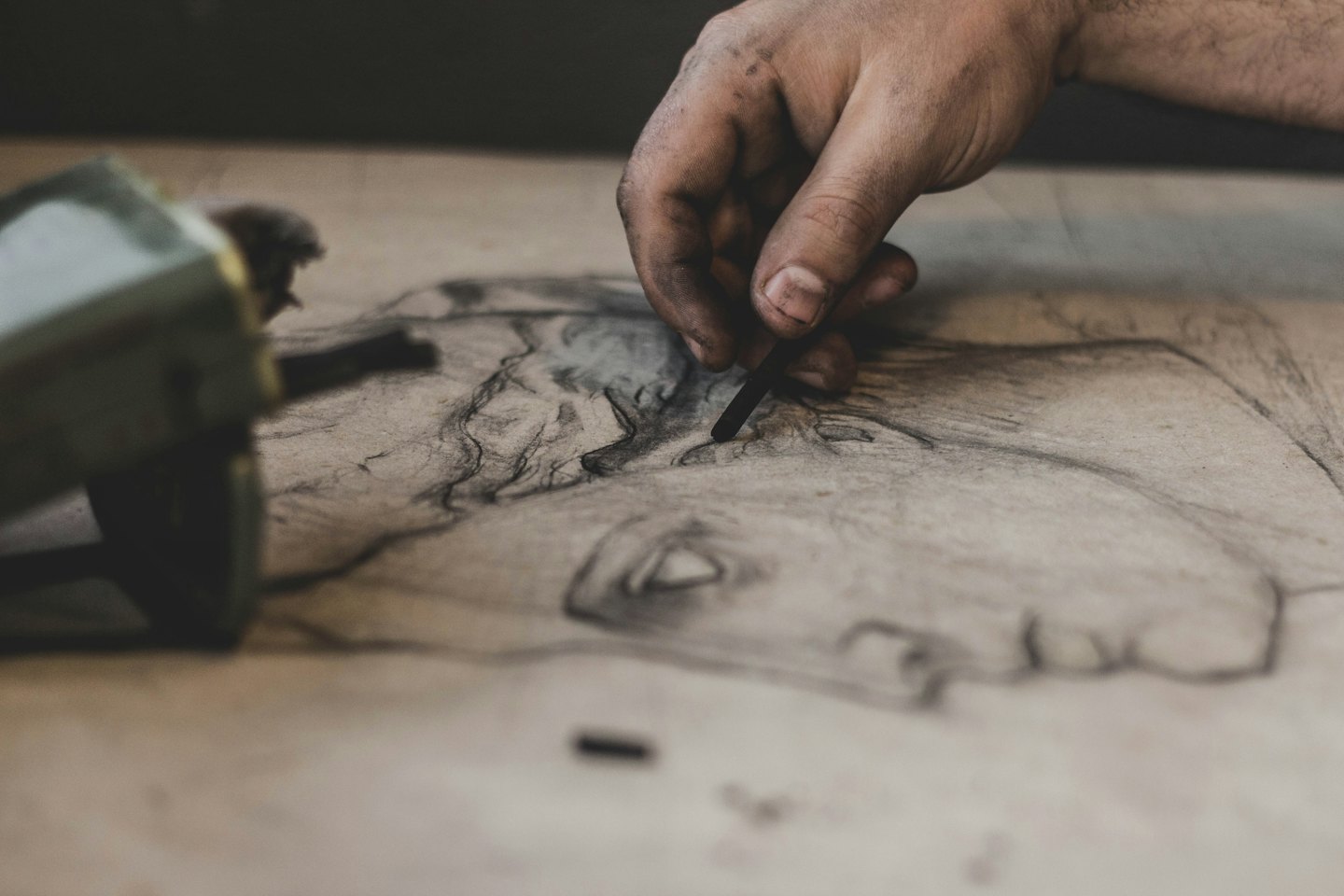 Artist's hand drawing a portrait with charcoal on paper.