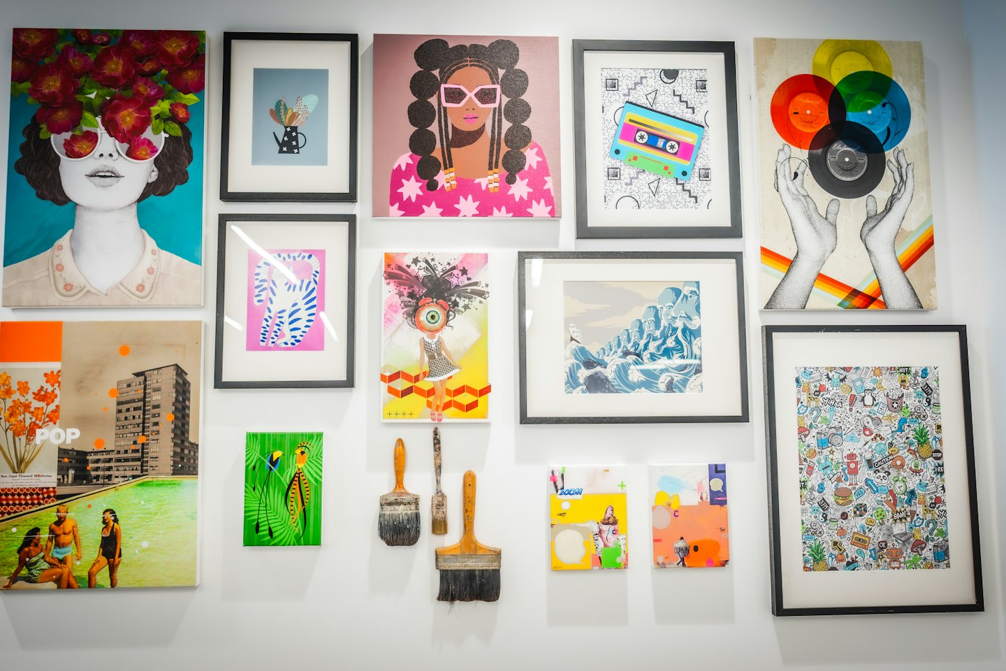 Eclectic collection of contemporary artwork and paintbrushes on a gallery wall.